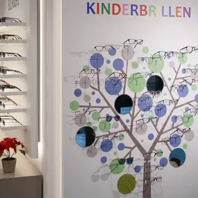 Bunte Kinderbrillen werden auf einem Baum-Display in einem modernen Optikergeschäft präsentiert.