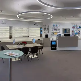 Modernes Optikergeschäft mit Brillenregalen, Beratungstischen und Empfangstheke.